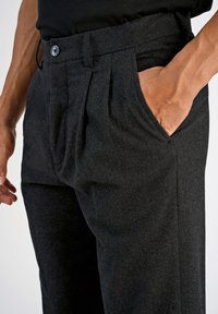 Skräddarsydda svarta byxor i en texturerad tygkvalitet, med rynkad front, sidofickor och knappstängning i midjan.