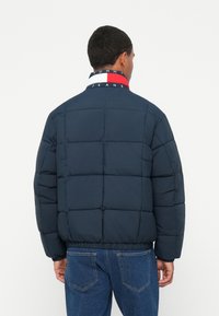 Chaqueta acolchada azul marino con un diseño de quiltado, pu�ños y dobladillo elásticos. Presenta un cuello en rojo, blanco y azul con la marca.