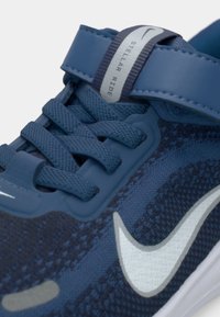 Μπλε αθλητικό παπούτσι με υφασμάτινο επάνω μέρος με υφή, έντονο λευκό swoosh και ασφαλή λουράκι πάνω από τη γλώσσα για επιπλέον στήριξη.