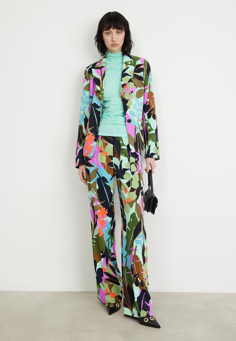 Garniturowy zestaw w kwiatowy wzór, składający się z kolorowego żakietu i spodni o szerokich nogawkach, w komplecie z miętową bluzką. Czarne czółenka oraz mała torebka.