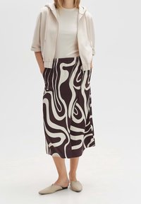 Dlouhá, vzorovaná sukně s vířivým béžovým a tmavohnědým designem, spárovaná se krémovou mikinou a béžovými nazouvacími botami.