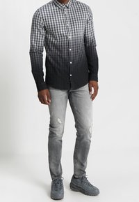 Camisa de botones con un patrón de cuadros que pasa de gris claro en la parte superior a gris oscuro, combinada con jeans claros desgastados y zapatillas grises.