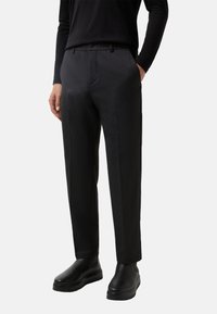 Pantalons ajustés gris en tissu lisse, avec une taille plate, des poches latérales et une coupe droite, assortis à des chaussures noires.