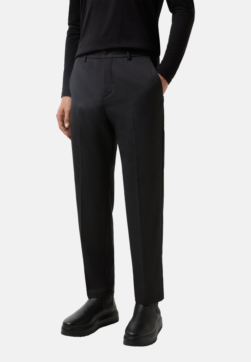 Pantalons ajustés gris en tissu lisse, avec une taille plate, des poches latérales et une coupe droite, assortis à des chaussures noires.