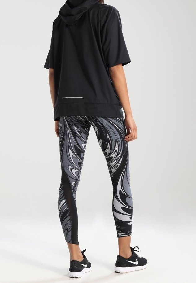 Černá krátká mikina s kapucí a reflexním detailem, spárovaná s legínami vysokého pasu s vířivým černobílým vzorem. Černé tenisky.