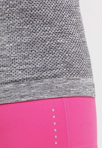 Top atletico grigio a motivo con un design testurizzato, abbinato a pantaloni corti atletici rosa lisci con punti grigi verticali sui lati.