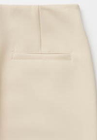 Beige tailored trousers featuring a smooth texture, a stitched back pocket, and a clean, minimalist design. No visible hardware or patterns.