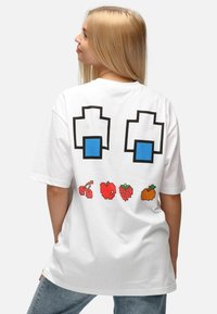 Camiseta blanca de gran tamaño con gráficos en estilo pixel: formas azules y cinco diseños de frutas coloridas impresas en la parte posterior.