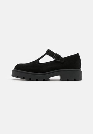 Chaussure Mary Jane en daim noir avec semelle à crampons épaisse et bride à boucle réglable, présentée en profil latéral sur fond blanc.