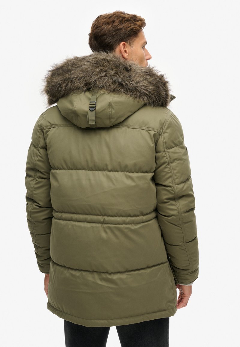 Chaqueta de plumas verde oliva con capucha forrada de piel sintética, puños acanalados y acolchado cosido, que cuenta con cordones ajustables y una textura suave.