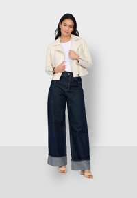 Crème faux leren jas, witte t-shirt en wijde donkere spijkerbroek met opgerolde mouwen, gecombineerd met naakt kleur blokhak sandalen.