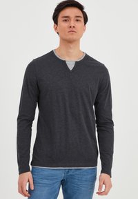 Mørkegrå langærmet skjorte med V-hals, der har en kontrasterende grå halsudskæring og en blød tekstur, parret med lyseblå jeans.