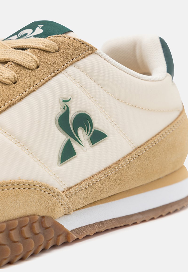 Baskets avec une tige en nylon beige, des accents en daim beige et un logo vert. Présente une semelle en caoutchouc avec un motif pour une bonne adhérence.