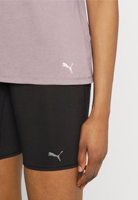 Camiseta de algodón morada de mangas cortas con logo blanco, combinada con Shorts elásticos negros que tienen un logo gris en el dobladillo.