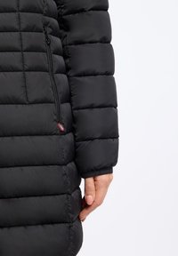 Zwarte pufferjack met een gewatteerde textuur, ritszakken aan de zijkant en elastische manchetten. Gemaakt van soepel, lichtgewicht materiaal, ontworpen voor warmte.