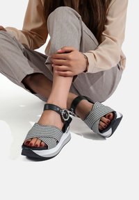 Sandali intrecciati in bianco e nero con suola spessa bianca, dotati di un accento di gemma sulla cinghia alla caviglia e design a bande incrociate per una vestibilità sicura.