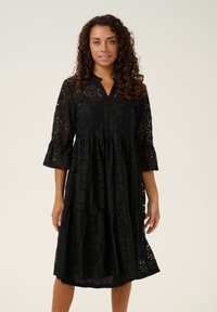Black lace dress featuring a v-neck, three-quarter flared sleeves, and tiered skirt with intricate patterns and a lightweight texture.