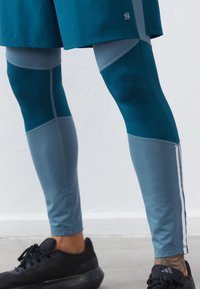 Τιρκουάζ και ανοιχτό μπλε αθλητικά κολάν με υφασμάτινα σχέδια, αντίθετους πανάρχες και μια ανακλαστική λωρίδα κατά μήκος της πλευράς.