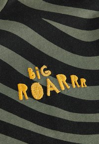 Zeleno-�čierna pruhovaná látka s vyšitým textom "BIG ROARRR" v žltej farbe. Text má textúrovaný, hravý dizajn.