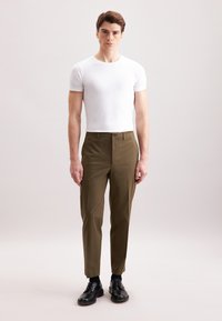 Camicetta bianca a maniche corte, aderente. Pantaloni verde oliva con taglio dritto, texture liscia. Scarpe nere stringate completano l'outfit.