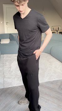 Černé tričko s výstřihem do V, spárované s černými tepláky s vyšitým logem. Volný střih s hladkou texturou látky, doplněné o šedé tenisky.