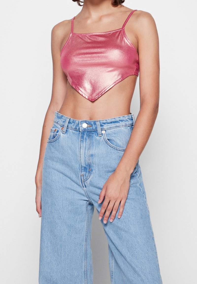 Top recortado brillante de color rosa con tirantes finos, que presenta un dobladillo en punta. Adornado con una textura suave, combinado con unos pantalones vaqueros de tiro alto en azul claro.