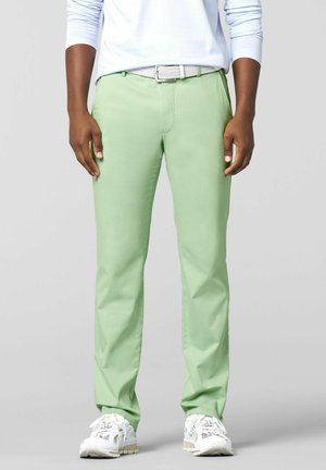 Person wearing light green pants, white belt, white long-sleeve shirt, and white sneakers standing against a plain background.