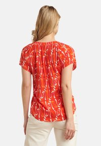 Rode blouse met patroon en korte mouwen, heeft een geplooide halslijn en een draaiend abstract ontwerp in wit en roze, gemaakt van lichtgewicht stof.