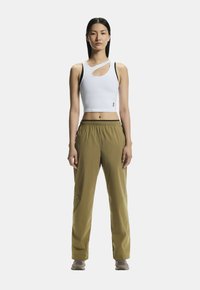 Weißes, kurzes Tanktop mit Ausschnitt, kombiniert mit lockeren, olivgrünen Hosen mit elastischem Bund und seitlichen Taschen. Graue Schuhe.
