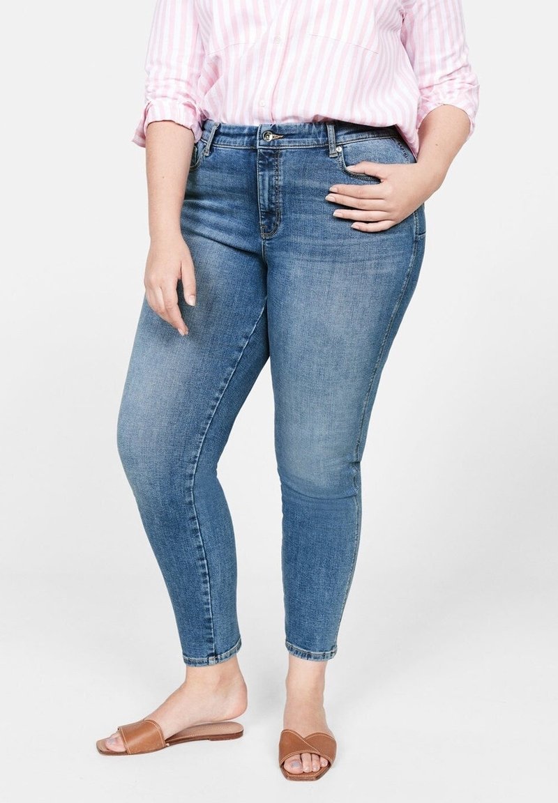 Jean skinny en denim bleu clair avec un lavage légèrement délavé, doté d'une poche avant et d'une braguette zippée, associé à des sandales marron à enfiler.