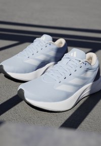 Hellblaue Sportschuhe mit einem atmungsaktiven Mesh-Obermaterial, weißer Gummisohle und dezenten grauen Akzenten. Drei weiße Streifen an den Seiten.