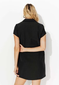 Robe noire avec un design à col, des manches courtes et une taille cintrée. Texture lisse, longueur genoux avec un léger évasement en bas.