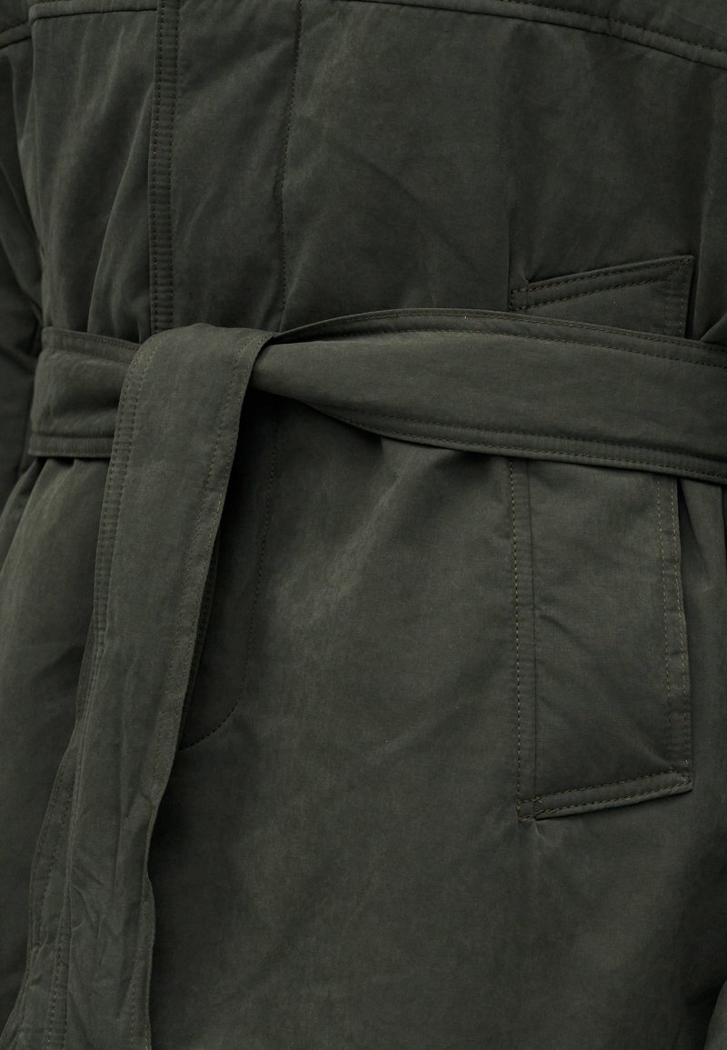 Donkergroene stoffen jas met een brede riem die om de taille is geknoopt en een zichtbaar gestikte zak met klep.