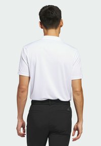 Witte polo met korte mouwen en kraag, gemaakt van gladde stof, gecombineerd met zwarte broek met een gestructureerde riem en twee achterzakken.