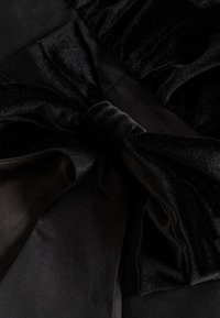 Robe en velours noir mettant en avant un détail de nœud prononcé, avec une texture douce et des accents en satin lisse, mettant en valeur un design élégant et raffiné.