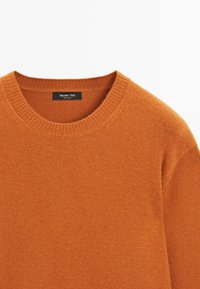 Pomarańczowy sweter z dzianiny z okrągłym dekoltem, o delikatnej fakturze i prążkowanymi detalami wokół kołnierza. Widoczna metka marki wewnątrz.