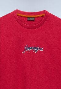 Rød T-shirt med rund hals, orange kant indvendigt på kraven og "Napapijri" logo i blåt og hvidt skrift midt på brystet.