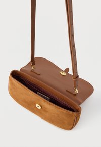 Brūna ādas somiņa ar zābakveida apakšu, zelta sprādzi un regulējamu siksnu. Iekšpusē ir dziļi sarkana oderējuma.