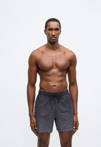 Črne kopalne kratke hlače z subtilnim geometrijskim vzorcem, elastičnim pasom in vrvico, narejene iz lahkega, hitro sušečega materiala.