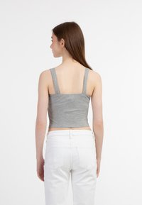 Grå ribbet crop top med brede stropper, tætsiddende design og strækbart stof. Kombineret med hvide højtaljede jeans, der fremhæver et afslappet look.