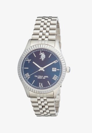 Montre-bracelet à bracelet en métal argenté avec cadran bleu, chiffres romains, fenêtre de date à 3 heures, logo et texte U.S. Polo Assn. sur le cadran.