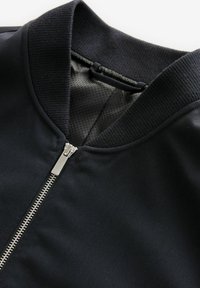 Chaqueta bomber negra con cierre de cremallera, cuello acanalado y forro texturizado. Tejido suave con un acabado mate y cremallera en contraste.
