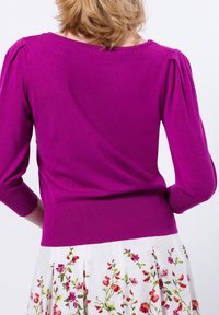 Fuksia neulepaita, jossa on kolmen neljänneksen hihat, istuva vyötärö ja teksturoitu pinta. Yhdistetty valkoiseen hameeseen, jossa on värikkäitä kukkakirjontoja.