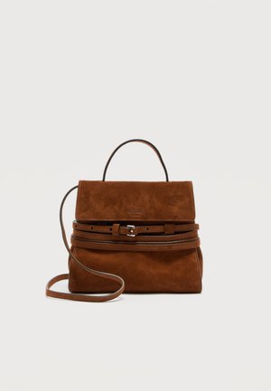 Brūna zamšādas rokas soma ar augšējo rokturi, regulējamu jostas detaļu priekšpusē un garu plecu siksnu uz vienkārša gaiša fona.