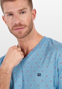 Camicia a V blu a motivo, realizzata in tessuto traspirante, con piccole forme di diamante in rosso e blu navy, e un logo ricamato sul petto.
