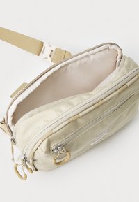 Beige Nylon Umhängetasche mit mehreren Reißverschlussfächern und einem hellen Innenraum, ausgestattet mit einem kleinen weißen Logo und einem verstellbaren Gürtel.