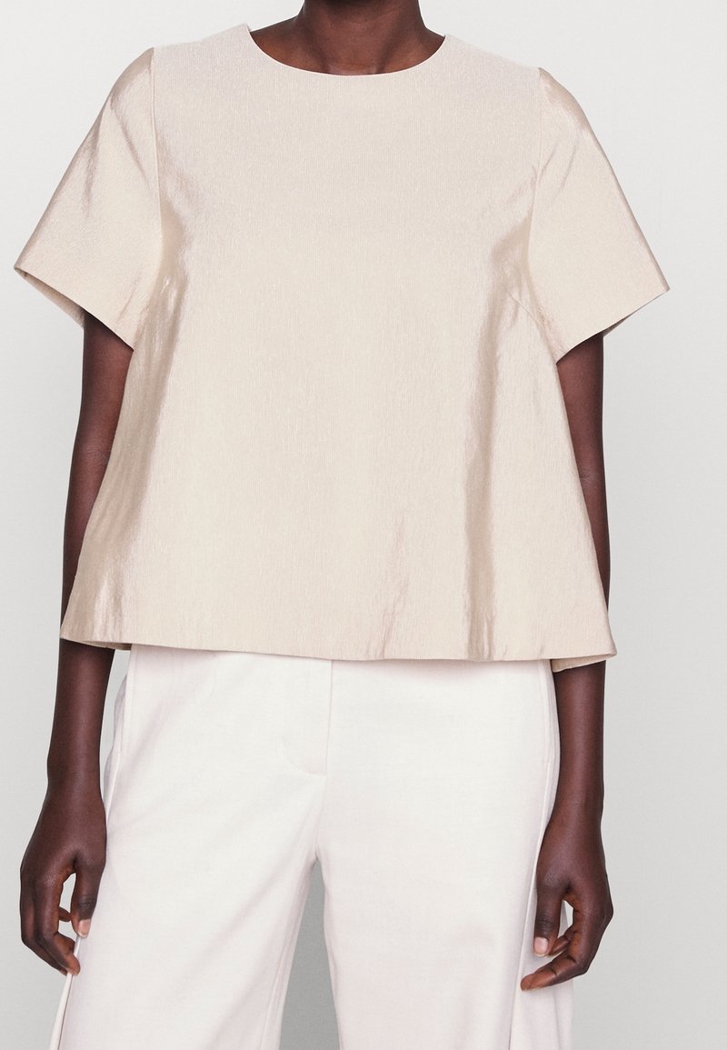 Beige, teksturoitu paita, jossa on lyhyet hihat, väljä istuvuus ja pyöreä pääntie. Yhdistetty vaaleanvärisiin, leveälahkeisiin housuihin.