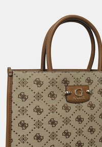 Sac à main en toile beige avec des accents en cuir brun, motif en losange, plaque logo métallique et double anses. Design rectangulaire compact.