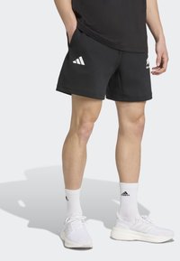 Sorte træningsshorts med to sidelommer, lige snit og hvide Adidas-logo detaljer foran. Båret med hvide træningssko og sokker.
