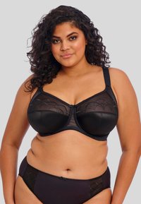 Sutiã preto com sobreposição de malha e detalhes em escalope, suporte com aro e alças ajustáveis. Conjunto inclui cuecas pretas e cinzas escuras combinadas.